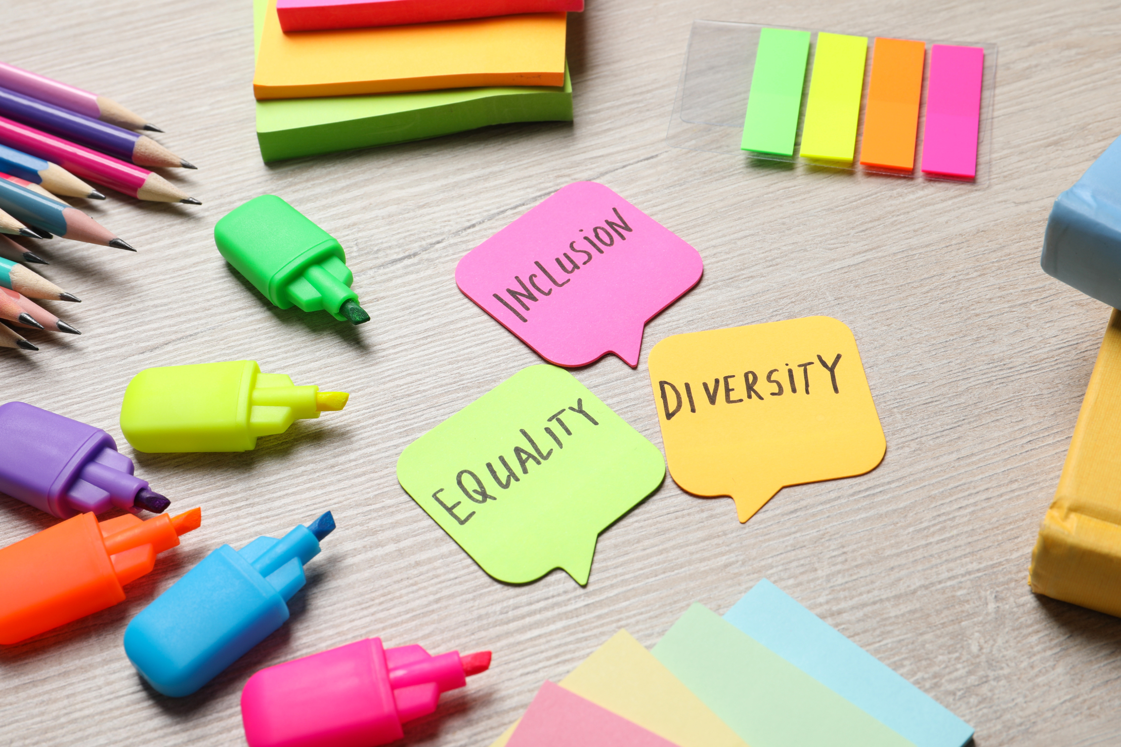 Auf dem Symbolbild sind Notizzettel, Textmarker-Stifte, Bleistifte in verschiedenen Formen und neonfarben abgebildet. In der Mitte finden sich die Worte Diversity, Equity, Inclusion auf je einem sprechblasenförmigen Notizzettel.